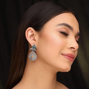 May include: Silver tone dangle earrings with a teardrop-shaped pendant and green gemstone accents.