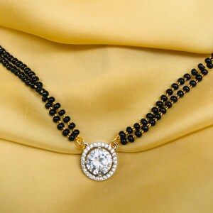 May include: A gold chain necklace with a large, round, clear stone pendant surrounded by smaller stones. The chain is made of black beads.