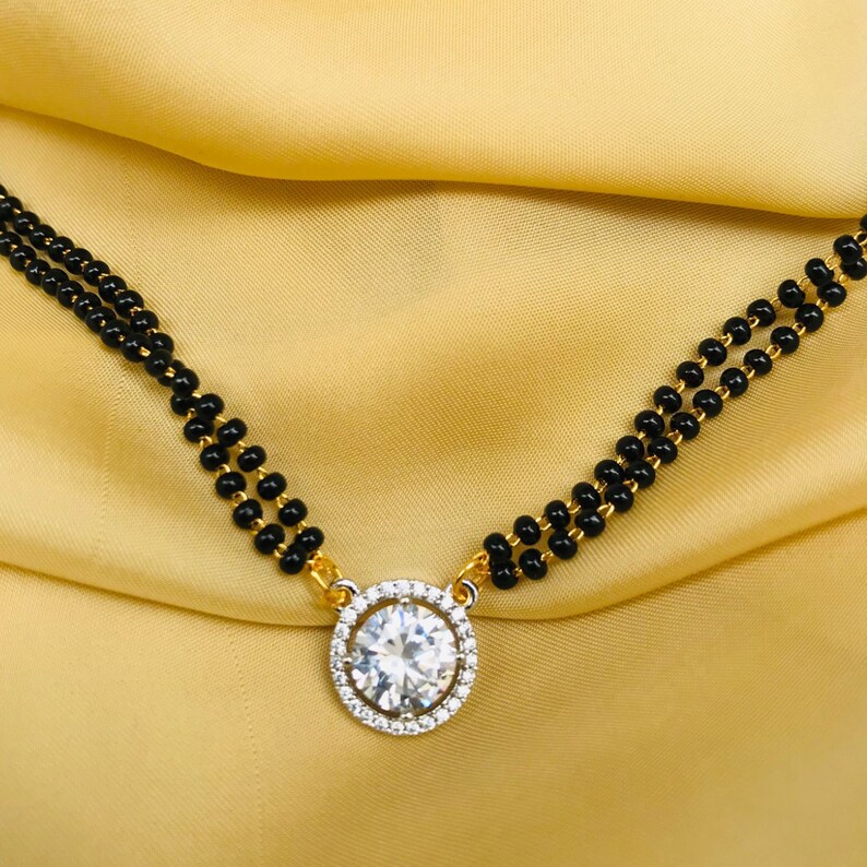May include: A gold chain necklace with a large, round, clear stone pendant surrounded by smaller stones. The chain is made of black beads.