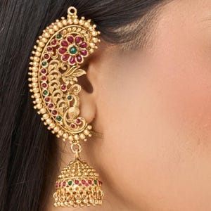 May include: Gold ear cuff with a peacock design and red and green gemstones. The cuff has a dangling bell charm with additional red and green gemstones.