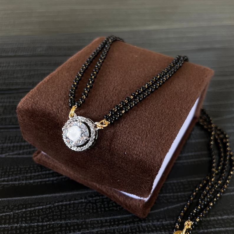 May include: A black beaded necklace with a gold pendant featuring a large, clear, round stone surrounded by smaller stones.