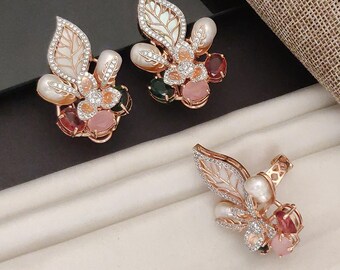 May include: A set of three rose gold-toned jewelry pieces. Two are earrings, and one is a pendant. Each piece features a leaf design with white enamel, clear crystals, and colorful gemstones in pink, green, and red.