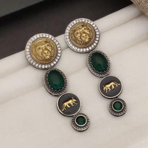 May include: Earrings in gold and silver tones, with lion and panther motifs. The earrings incorporate green oval and round gemstones. Some have a lion's head, others a panther silhouette. The designs are intricate.