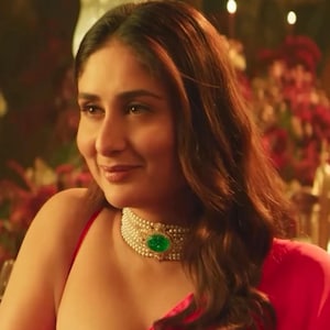 May include: A woman wearing a red dress and a pearl necklace with a large green gemstone. The necklace is a choker style, and the woman has brown hair.