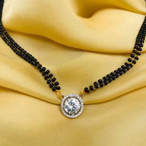 May include: A black beaded necklace with a gold pendant featuring a large, round, clear stone surrounded by smaller stones.