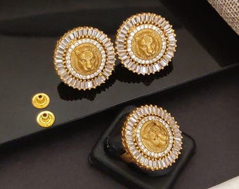 May include: Gold-toned jewelry set featuring a ring and two pairs of earrings. Each piece showcases a lion's head in the center, surrounded by clear, rectangular and round-cut crystals. The earrings and ring are displayed on a black surface.