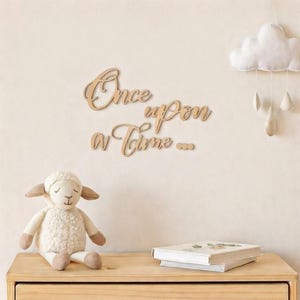 May include: Wooden wall art spelling "Once upon a time..." in cursive script. A plush sheep toy sits on a wooden surface with a stack of books. A white cloud with hanging teardrops decorates the wall, creating a nursery theme.