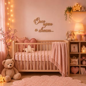 Könnte beinhalten: Ein hölzernes Wandschild mit dem Text Once upon a dream, ein helles Holzbettchen mit einem rosa geblümten Laken, ein herzförmiges rosa Kissen, ein sternförmiges Kissen, eine rosa Decke, ein großer Teddybär und ein rosa Teppich.
