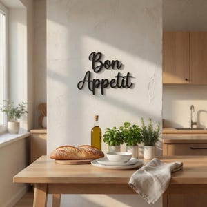 May include: A wooden kitchen table with a loaf of bread, plates, and a linen napkin. A bottle of olive oil and potted herbs are also on the table. The wall features a black "Bon Appetit" sign.