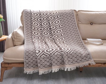 Puede incluir: Una manta de tiro de color marrón y blanco con flecos sobre un sofá beige.