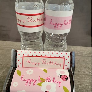 May include: Two clear plastic water bottles with pink and red labels that say "happy birthday". Two chocolate bars wrapped in pink and white paper with red polka dots and the text "Happy Birthday" and "happy birthday".