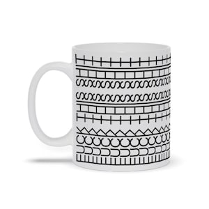 May include: White ceramic coffee mug with a black geometric pattern. The design features horizontal bands of lines, curves, and shapes. The mug has a white handle and is suitable for hot or cold beverages.