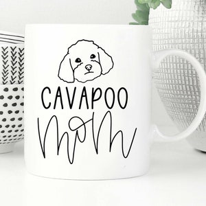 Op de afbeelding: Witte keramische mok met een zwarte lijntekening van een cavapoo-hond en de tekst "Cavapoo Mom" in zwart.