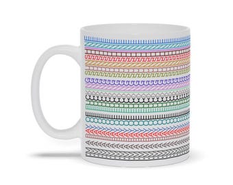 Peut inclure: Tasse à café en céramique blanche avec un motif coloré. Le motif présente des rangées horizontales de diverses formes et lignes dans des tons de bleu, rouge, jaune, vert, violet et noir. La tasse a une anse blanche et un intérieur blanc.