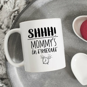 May include: White ceramic mug with black text that reads "Shhh! Mommy's in Timeout" and a black and white illustration of an alarm clock.