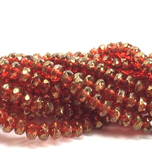 May include: Close-up of a strand of faceted, reddish-brown beads. The beads have a metallic sheen and are strung together, creating a textured, glittering effect. The beads are likely used for jewelry making.