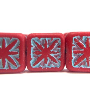 May include: Three red square beads with a blue floral design. The beads are made of ceramic and have a glossy finish.