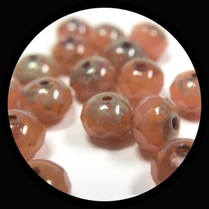 May include: A collection of small, round, faceted beads in a soft peach or light coral color. Each bead features a central hole and a subtle, iridescent metallic finish on the upper surface, creating a reflective sheen across the faceted edges.