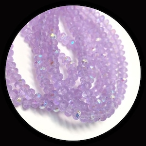 May include: A strand of small, faceted, light purple crystal beads. Each bead features a translucent finish with subtle iridescent highlights that catch the light, creating a shimmering effect along the entire length of the circular string.