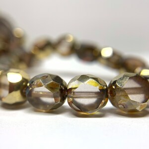 May include: A strand of faceted glass beads in a light brown color. The beads are round and have a shiny, metallic finish.