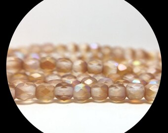 May include: A strand of faceted, round, light brown beads with a translucent, iridescent finish. The beads are arranged in a horizontal line, showing a reflective surface and a soft, warm color palette with subtle hints of shimmer.