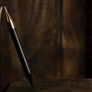 May include: A black knitting needle with a gold tip, resting on a wooden surface.