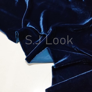 Op de afbeelding: Close-up van een diepblauwe fluwelen stof met een zachte, pluche textuur. De stof is gevouwen en gedrapeerd, wat de luxe uitstraling laat zien.