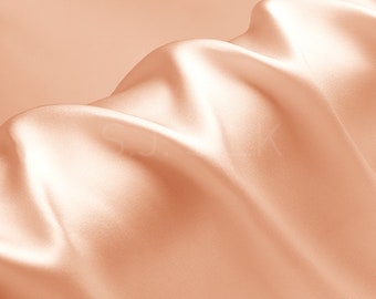 May include: A close-up of a smooth, peach-colored fabric with soft, flowing folds. The fabric has a subtle sheen and a luxurious feel.