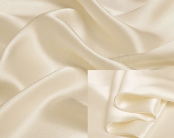 Puede incluir: Tela de seda de color crema con un acabado liso y brillante. La tela está drapeada y doblada para mostrar su textura.