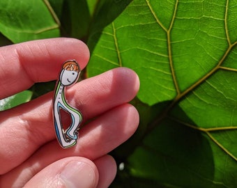 May include: A green, white, and orange enamel pin of a person in a yoga pose.