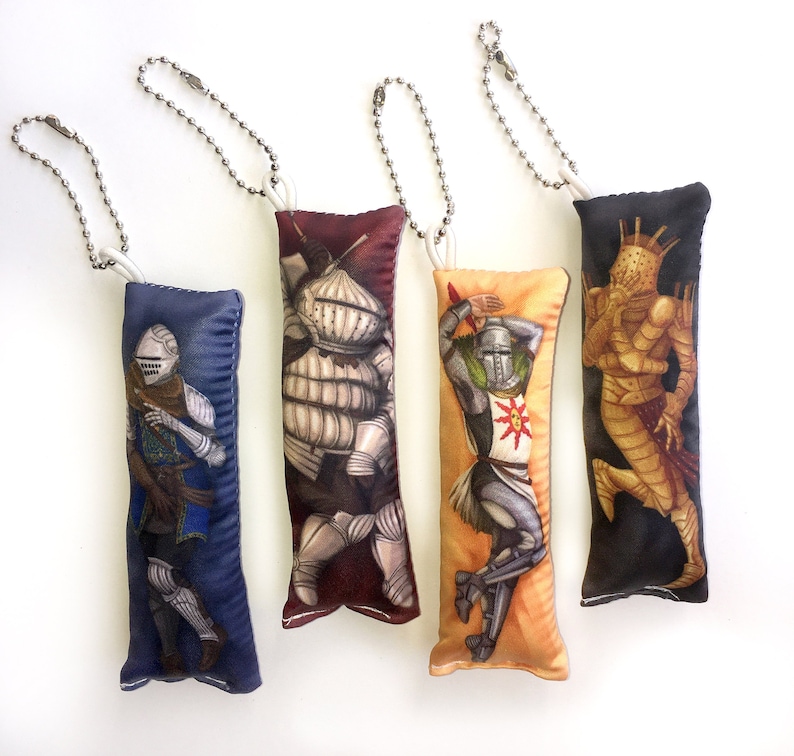May include: Four plush keychain pillows with different characters from the Dark Souls video game series. The pillows are all in different colors and feature detailed illustrations of the characters.