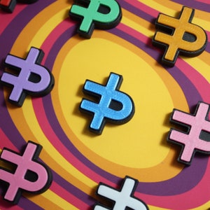 May include: A collection of colorful, plastic, dollar sign shaped ornaments. The ornaments are arranged in a circular pattern on a multi-colored, striped background.