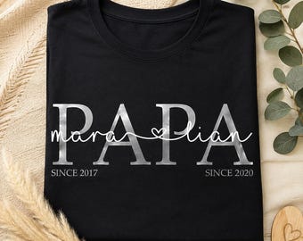 May include: A black t-shirt featuring the word PAPA in large silver letters. Overlaid in white cursive script are the names mara and lian connected by a heart. Below the names, the text reads SINCE 2017 on the left and SINCE 2020 on the right.