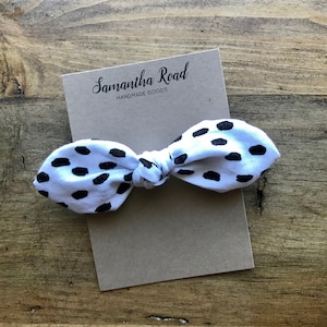 May include: A white fabric bow with black polka dots, tied in a knot. The bow is on a brown card with the text "Samantha Road Handmade Goods".