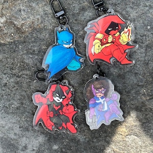 May include: Four superhero keyrings. The keyrings feature Batman in blue, a character in red, Batwoman in red and black, and a character in purple and blue. Each keyring has a black clasp.