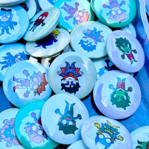 Puede incluir: Una colección de botones redondos, blancos, azules y morados con personajes de dibujos animados coloridos. Los personajes llevan diferentes atuendos y tienen diferentes expresiones.