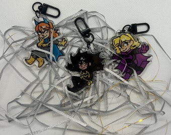 May include: Three colorful cartoon character keychains featuring a yellow-haired woman, a black-haired woman, and a blonde-haired woman. The keychains are made of clear acrylic and have black metal rings.