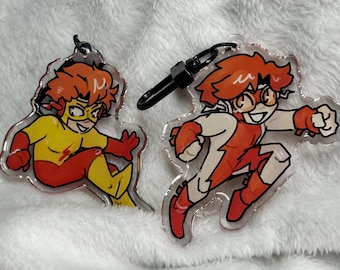 May include: Two acrylic keychains featuring a cartoon character in a running pose. One character is in a yellow and red suit, the other in a white and red suit. Both have orange hair and are smiling. Each keychain has a black clasp.