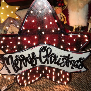 May include: A red and black plaid star-shaped sign with white lights and a white banner that says "Merry Christmas".
