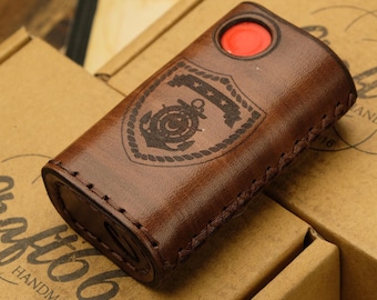 May include: A brown leather case with a stitched edge and a red button. The case has a laser-engraved design of a shield with a nautical anchor and the text "USCG". The case is sitting on a brown cardboard box with the text "Craftbb Handmade Est. 2016".