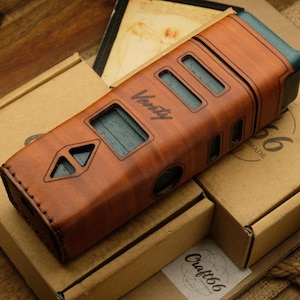 May include: A brown leather case with teal accents and the word "Varsity" is displayed on top of several cardboard boxes. The case has rectangular cutouts and a stitched design. The boxes are various sizes and shapes.