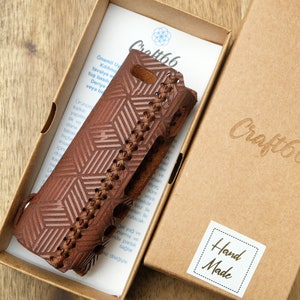 Puede incluir: Una funda de teléfono de cuero marrón con un patrón geométrico y costuras. La funda está en una caja con el texto "Craft66" y "Hand Made" impreso en ella.