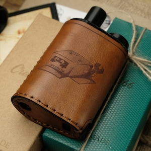May include: A brown leather case with a stitched edge and a design of a van with the text "Day-Smith" on the side. The case is sitting on a green box with a brown string tied around it.