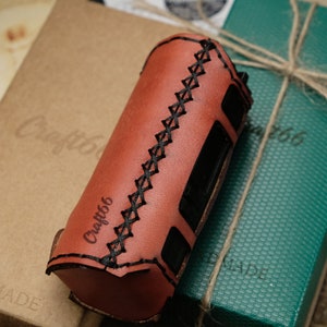 Puede incluir: Una funda de cuero marrón con costuras negras y el texto "Craft66" grabado en relieve en el lateral. La funda está sobre una caja marrón con el texto "Craft66" y "Handmade" en ella.
