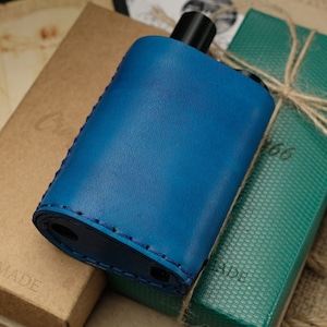 Peut inclure: Un porte-bouteille en cuir bleu avec un bord cousu. Le porte-bouteille est posé sur une boîte verte avec le mot "MADE" dessus. La boîte est enveloppée de ficelle.