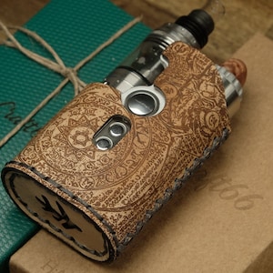 May include: A brown leather vape case with intricate engraved designs. The case has a stitched edge and a silver button. The case is sitting on a brown box with the word "Craft" written on it.