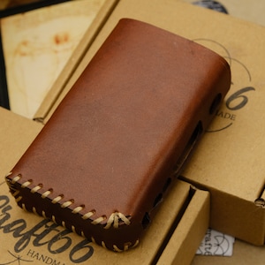 Puede incluir: Una funda de cuero marrón con costuras en los bordes. La funda está sobre una caja de cartón marrón con el texto "Craft 66 Handmade" impreso en ella.