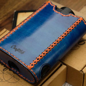 Puede incluir: Una funda de cuero azul con costuras naranjas. La funda tiene el texto "Craft66" grabado en la parte delantera. La funda está hecha a mano y tiene una etiqueta que dice "Handmade Est. 2016".