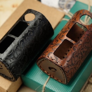 May include: Two leather cases with floral patterns. One is black, the other is brown. Both have cutouts for buttons and a circular opening. The cases are likely for a vape device or similar electronic gadget.