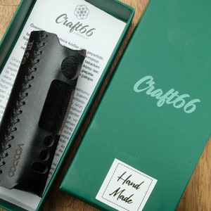 Puede incluir: Una funda de cuero negro con costuras y la palabra "VOOPOO" en relieve. La funda está en una caja verde con las palabras "Craft66" y "Hand Made" en ella.